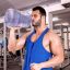 Мускулистый мужчина в спортзале пьет из галлонного кувшина с водой, как мифический гигант