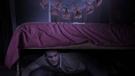 Человек спрятался под кроватью прикрыв рот, когда огромный вирус «стелс-омикрон» прорывался через его дом