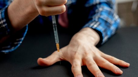 Скучающий работник вакцинации проводит вторую половину дня без пациентов, вонзая шприц между пальцами